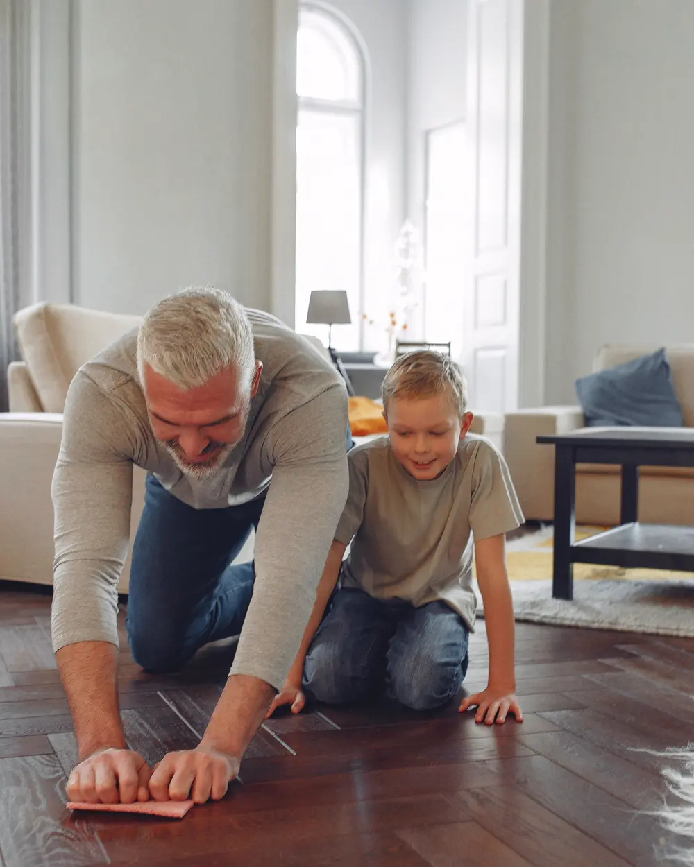Adult wiping a small area of a residential floor while a child watches