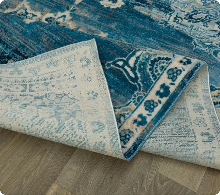 Folded blue patterned area rug showing its backing