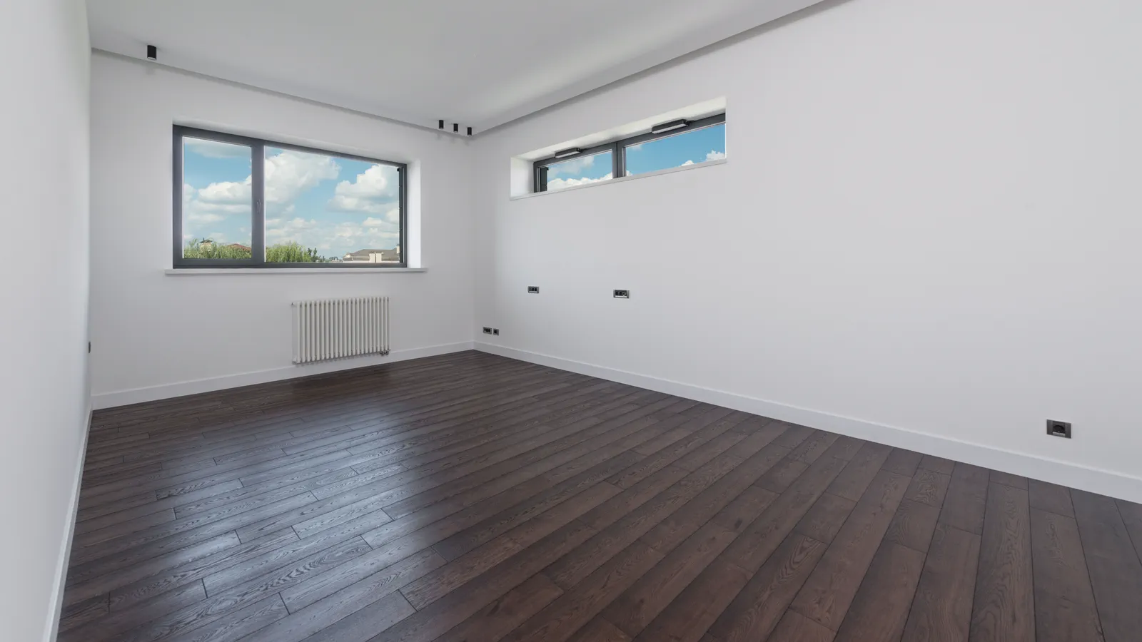 Empty modern room with dark wood-look plank flooring and white walls