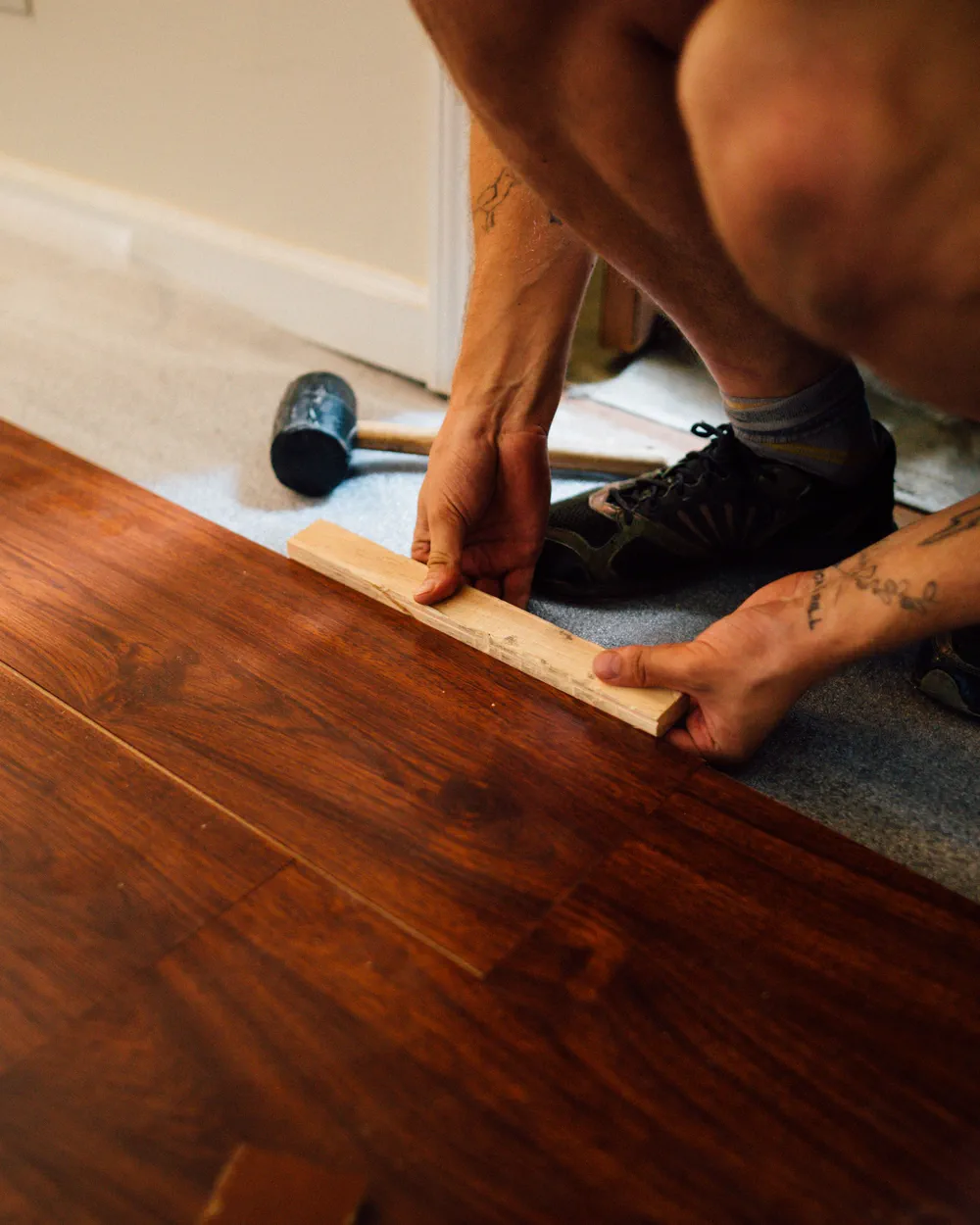 Worker fitting laminate planks with a tapping block and rubber mallet