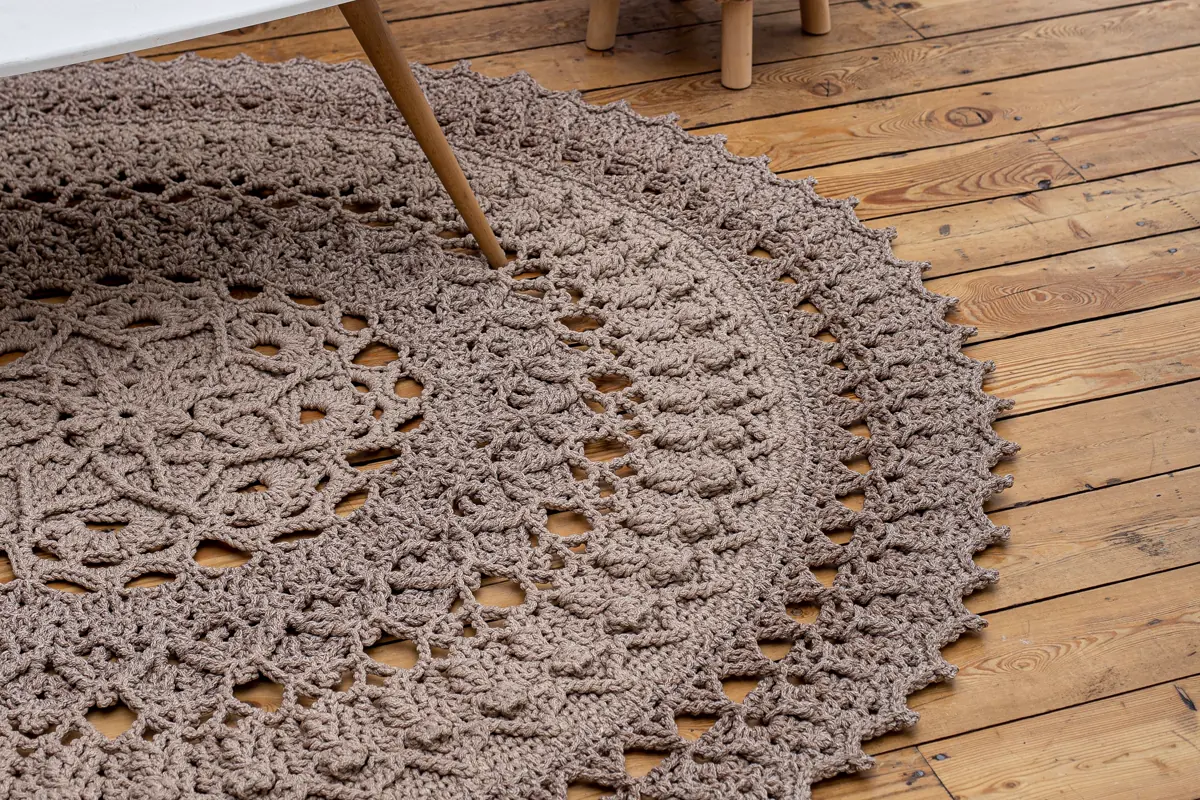 Close view of a textured crochet area rug beside exposed wood flooring