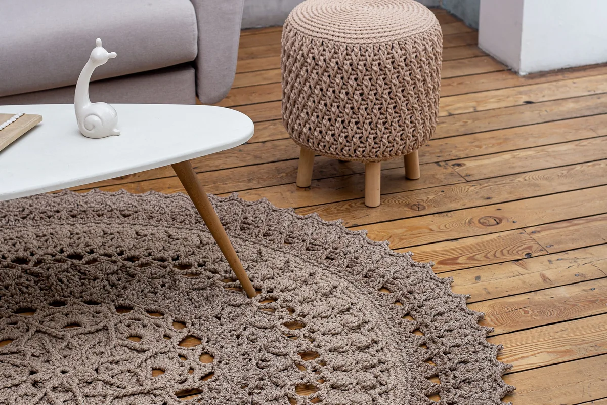 Textured crochet area rug beside exposed wooden floorboards and a knitted stool