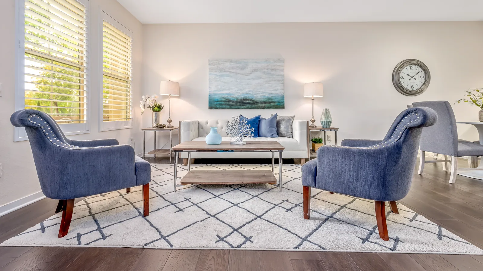 Blue armchairs and a white sofa arranged on a geometric area rug in a bright living room