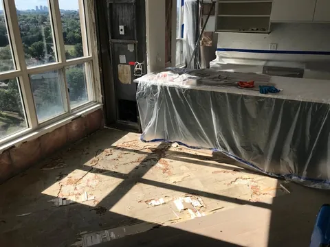 Partly removed glue-down floor with exposed adhesive beside the covered kitchen island, Toronto condo after a water leak