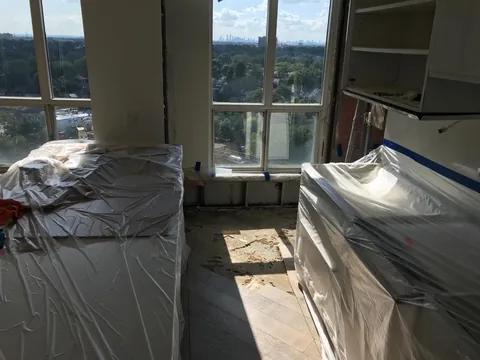 Kitchen cabinets and island wrapped in plastic while the water-damaged floor was removed, Toronto condo