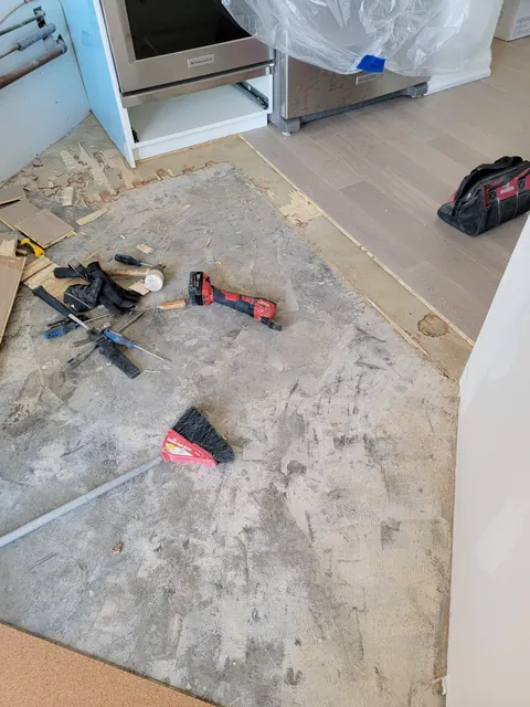 Subfloor partly scraped of old adhesive in front of the kitchen range, with tools on the floor
