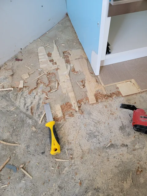 Scraping leftover glue-down flooring and adhesive off the subfloor at a kitchen cabinet corner